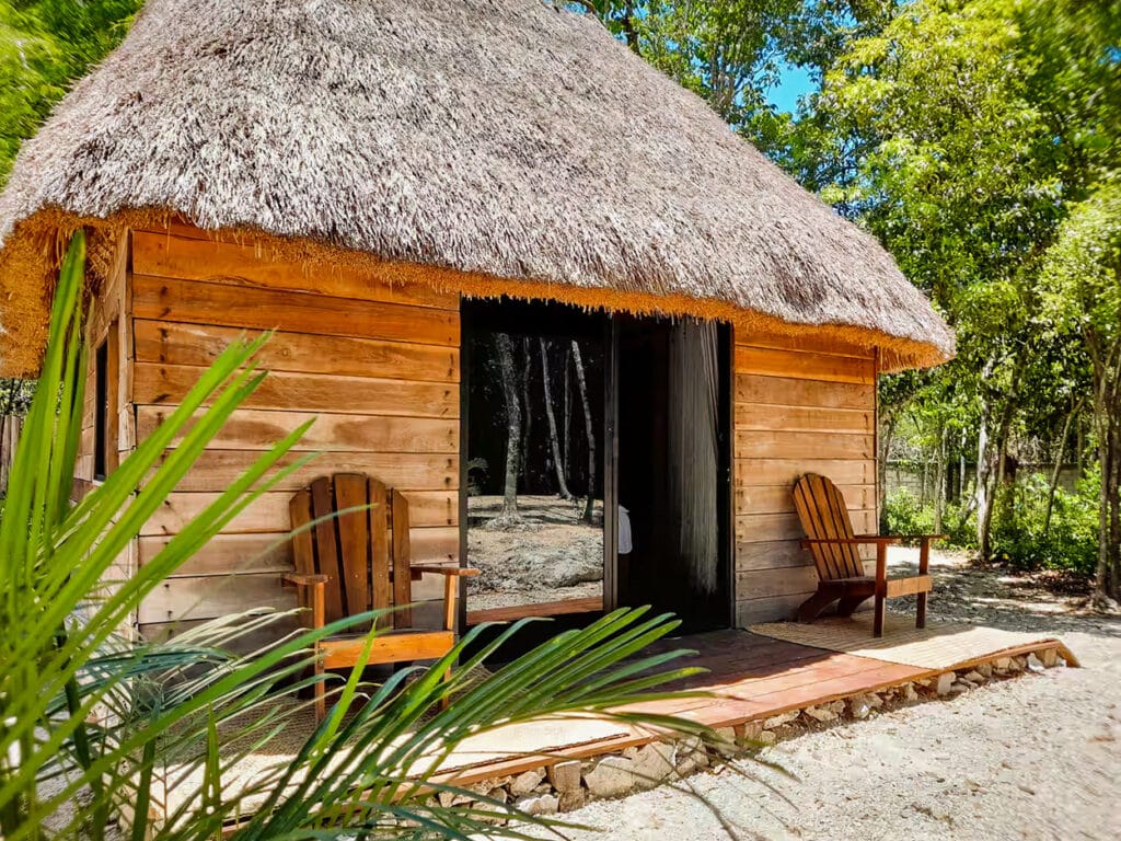 A cozy wooden cabin with a thatched roof surrounded by lush greenery at 10 Cabin Jungle Retreat in Puerto Aventuras, Xpu Ha area.