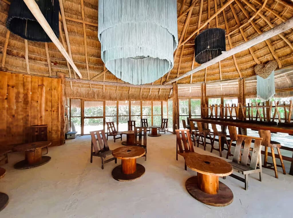 Interior view of the 10 Cabin Jungle Retreat in Xpu Ha, Puerto Aventuras, showing a spacious, open room with wooden furniture and a thatched roof.