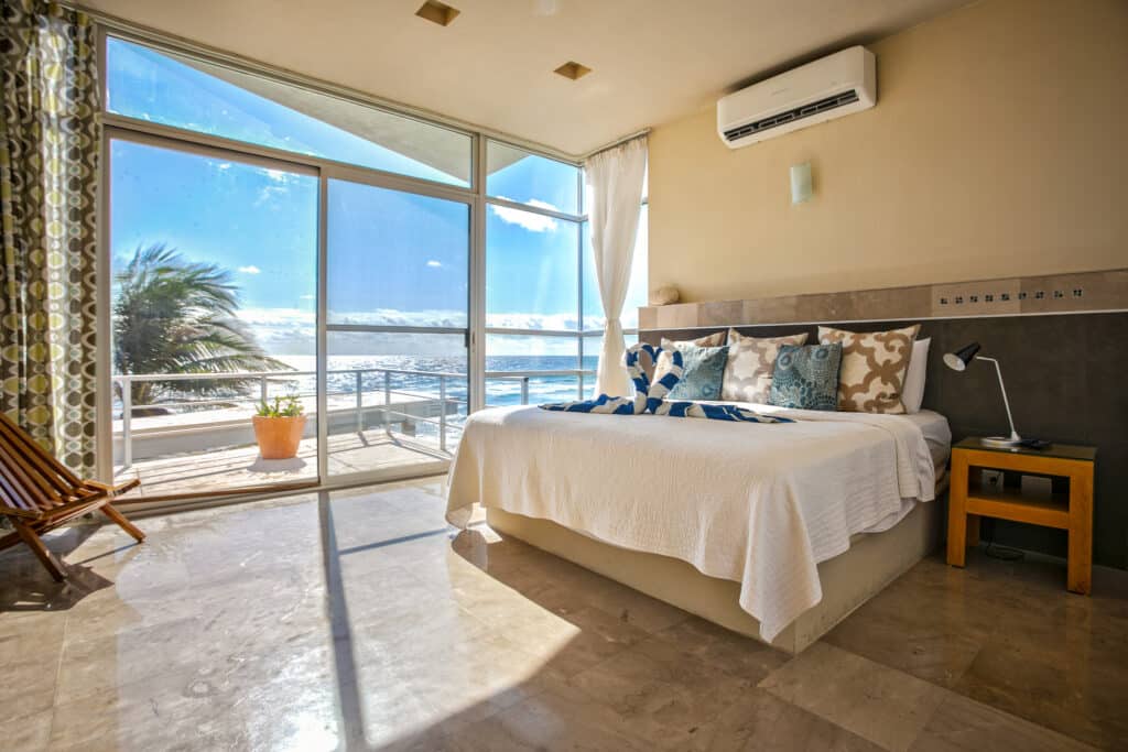 Bedroom in a beachfront house at Dos Bahias in Tulum with large windows offering ocean views and a towel folded into swan shapes on the bed.