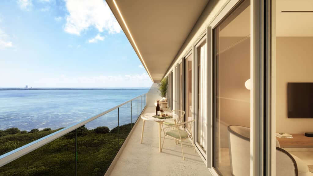 A spacious balcony overlooking the ocean at Bay View Grand in Cancun, with a small table, chairs, and a view of the sky, water, and lush greenery in the Grand Island area.