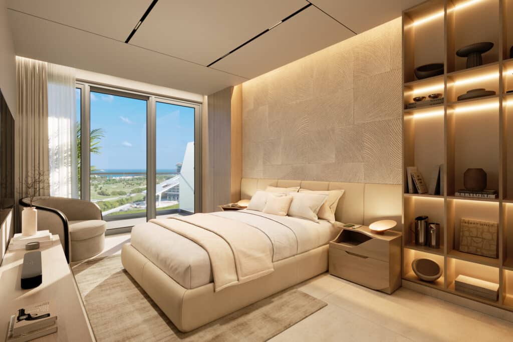 A modern bedroom in Bay View Grand 1419-B in Cancun's Grand Island, featuring a large window with ocean views, a beige bed, and built-in shelving with decorative items.