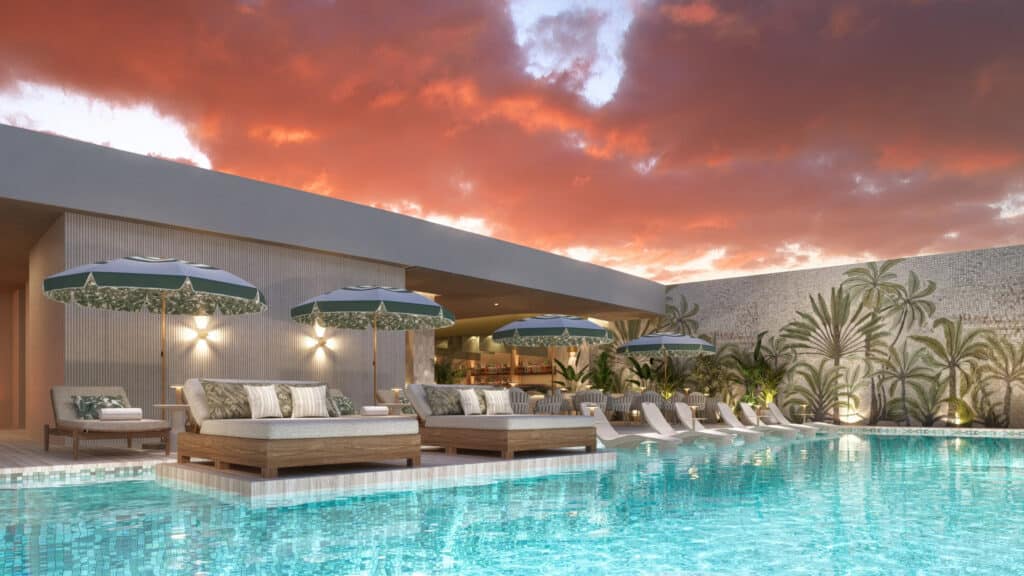 A luxurious pool area at Bay View Grand 1419-B in Cancun's Grand Island, featuring lounge chairs, umbrellas, and lush landscaping with a vibrant sunset sky.