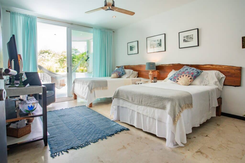 A bright bedroom in Bosque Los Aluxes Condo in Playa del Carmen, featuring with wooden headboards, a sliding glass door to a balcony, and simple wall art.