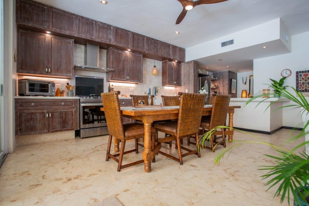 Interior view of Bosque Los Aluxes Condo in Playa del Carmen, showcasing a kitchen with wooden cabinets, a dining table, and natural light.