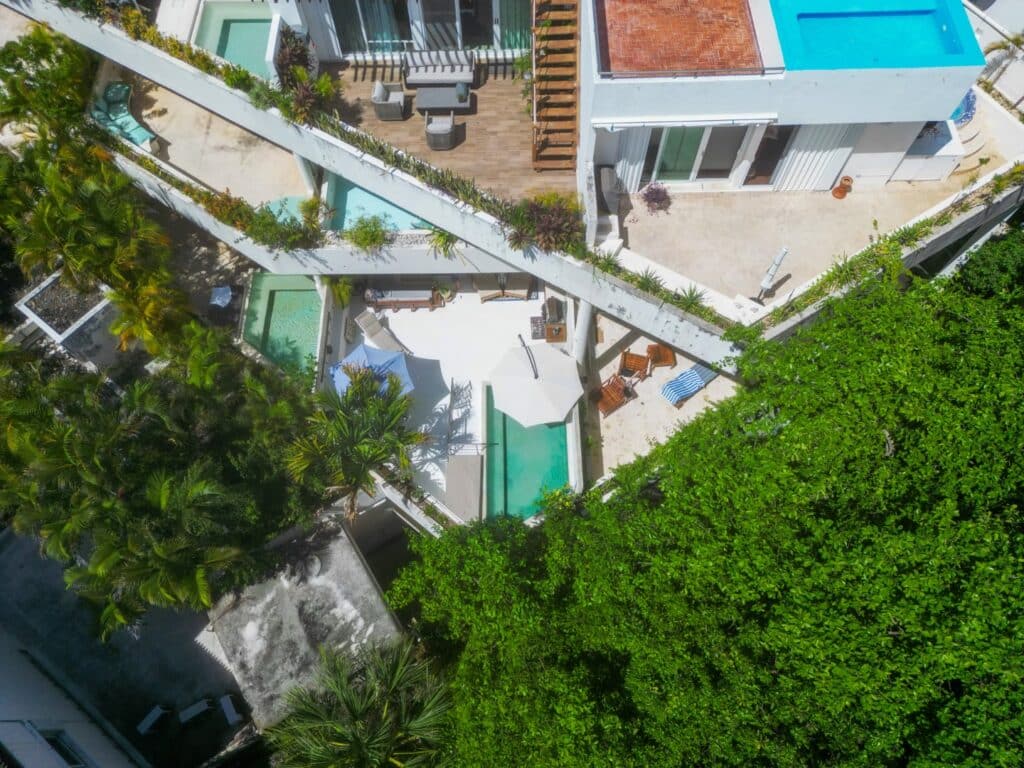 Aerial view of Bosque Los Aluxes Condo in Playa del Carmen's Centro area, showing a swimming pool, outdoor seating area, lush greenery, and surrounding buildings.