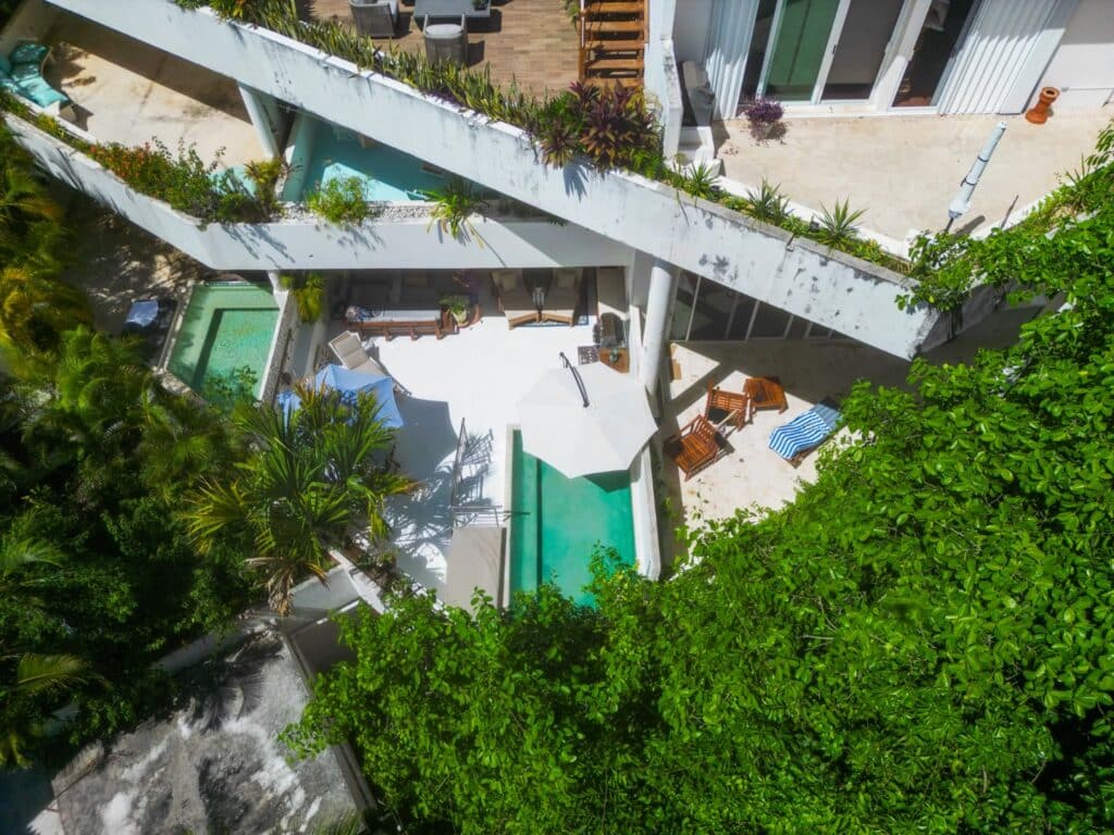 An aerial view of a condominium unit at Bosque Los Aluxes Condo in Playa del Carmen's Centro area, showing a private pool, outdoor seating, and lush greenery.