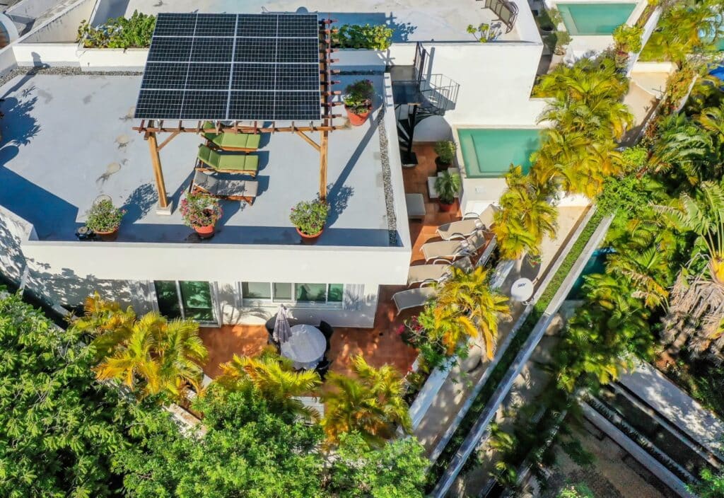 Aerial view of the Bosque Los Aluxes 301 Penthouse in Playa del Carmen, showing a rooftop terrace with a shaded seating area, potted plants, a small pool, and lush surrounding greenery.