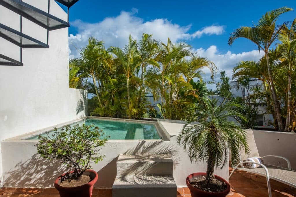 A view from Bosque Los Aluxes 301 Penthouse in Playa del Carmen, featuring a small pool with potted plants and palm trees on a sunny day in Centro Playa Del Carmen.