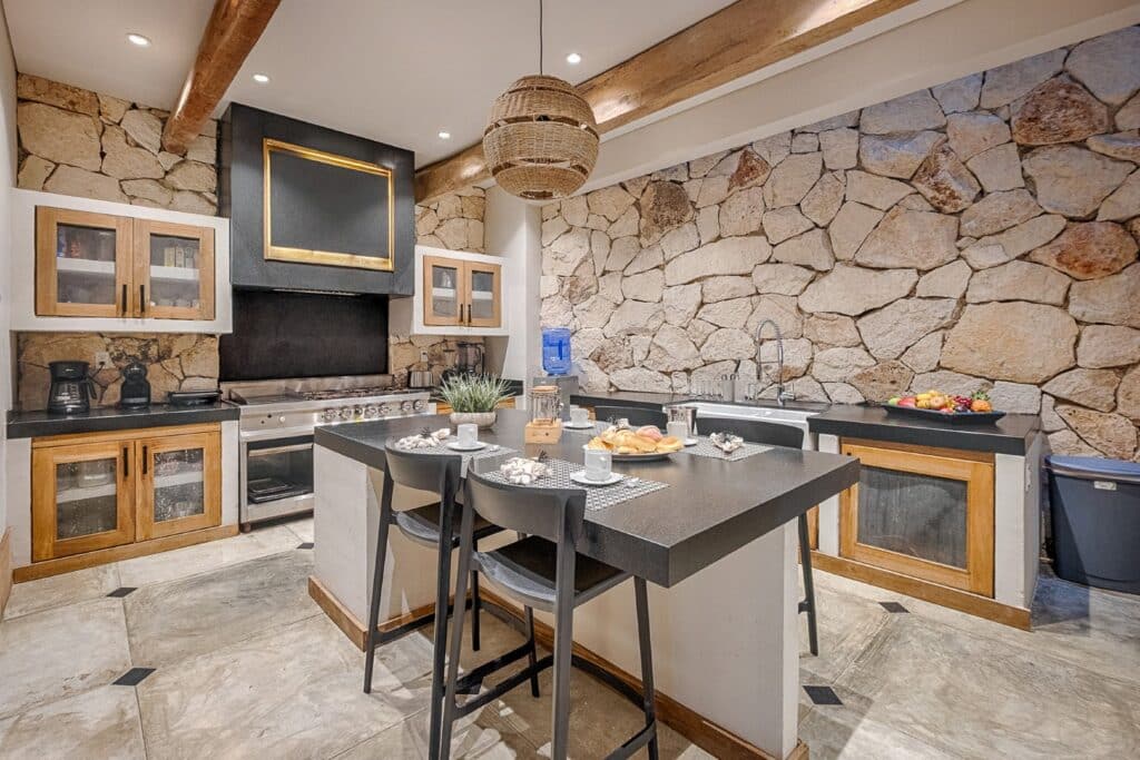 Modern kitchen in Villa Caleta, Puerto Aventuras, featuring a stone accent wall, black countertops, wooden cabinets, and a breakfast bar.