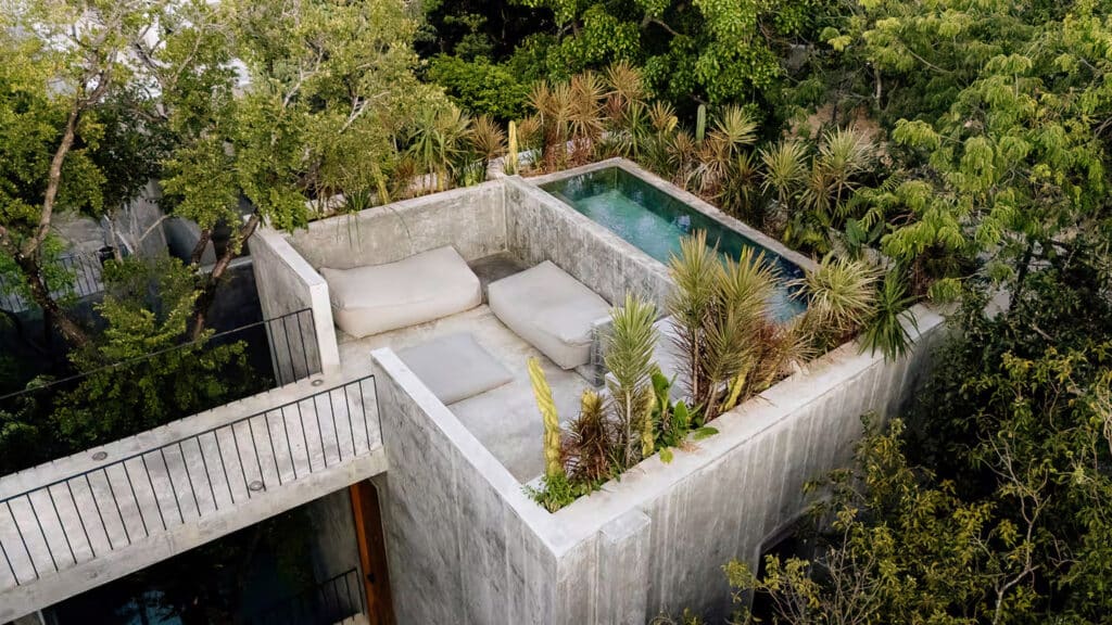 A rooftop pool with lounge seating surrounded by lush green trees at Casa Shalva in Aldea Zama, Tulum.