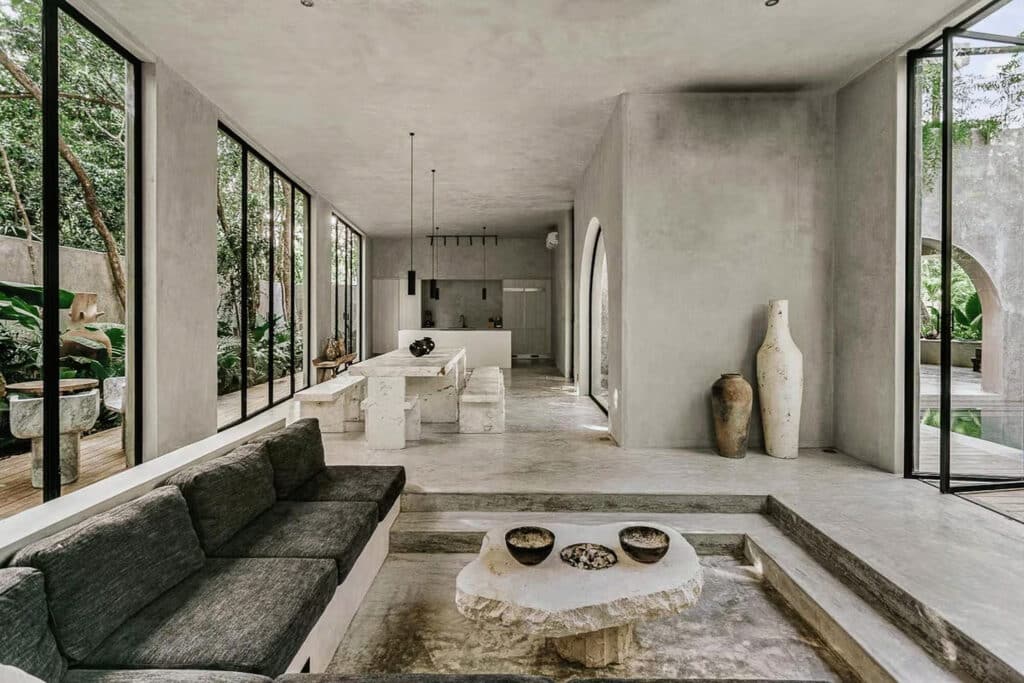 Interior view of Casa Shalva in Aldea Zama, Tulum, featuring minimalist concrete design, large glass windows, and natural decorative pottery.