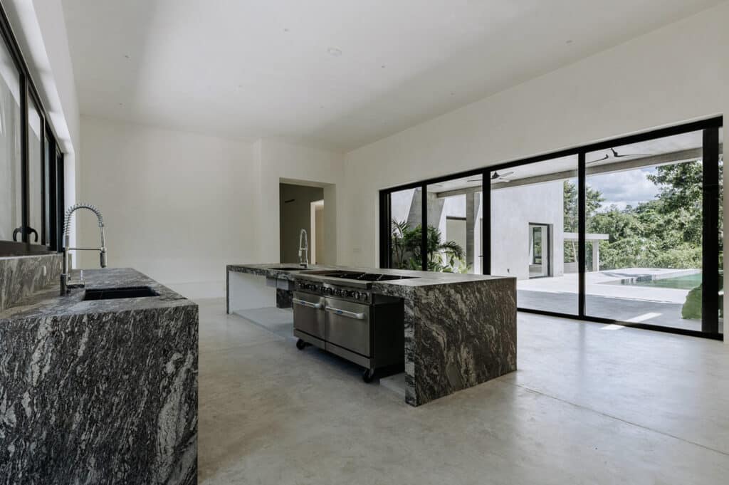 Modern kitchen in Villa Amanai Tulum House 5 with large sliding glass doors opening to outdoor greenery and pool area in Rancho Viejo, Tulum.