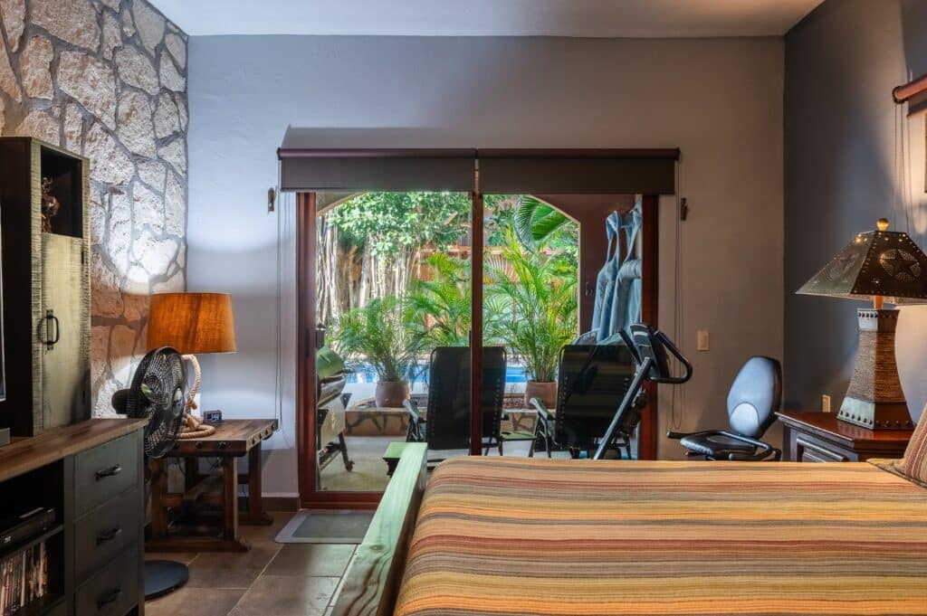 Interior of Villa Bonita Christies 44 in Casa Bonita, Playa del Carmen, showing a bedroom with a sliding glass door leading to a patio with lush greenery.