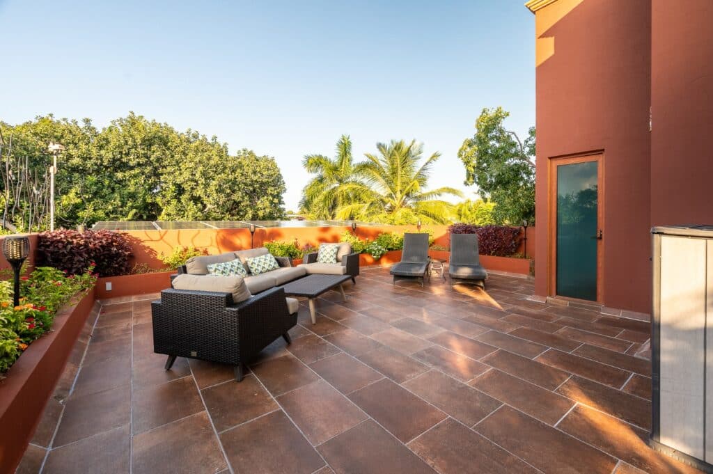 A spacious outdoor terrace at Casa Bonita in Playa del Carmen, featuring a comfortable seating area with lounge chairs, surrounded by lush greenery and vibrant sky.