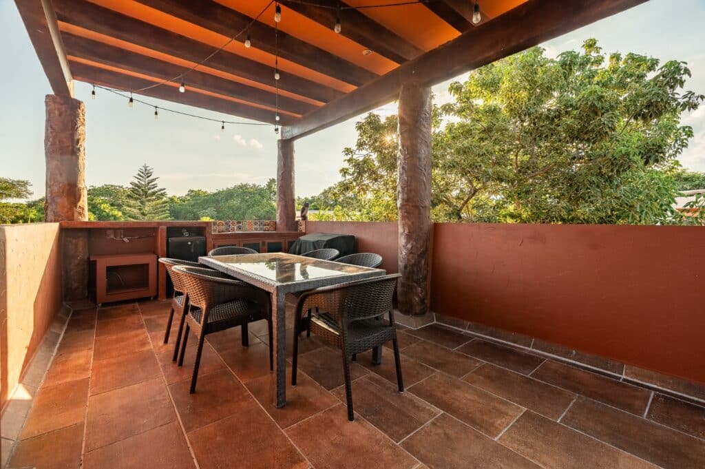 Outdoor terrace at Casa Bonita in Playa del Carmen, featuring a wooden ceiling, string lights, a dining table with six chairs, and views of lush green trees.