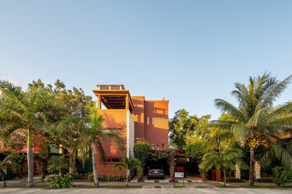 A modern orange and white villa with a rooftop deck, surrounded by lush palm trees in the El Cielo area of Playa del Carmen at Casa Bonita.