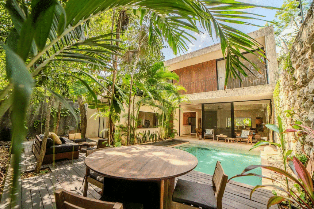 A modern villa with a swimming pool and outdoor seating area, surrounded by lush greenery at Villa Kaan in Holistika, Tulum.