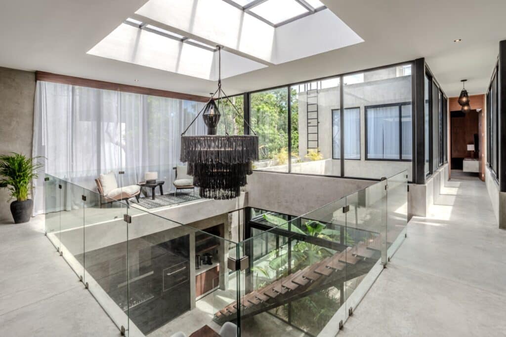 Interior shot of Villa Karmond, Tulum, featuring a modern open space with glass railings, a skylight, and minimalist furnishings overlooking the courtyard.