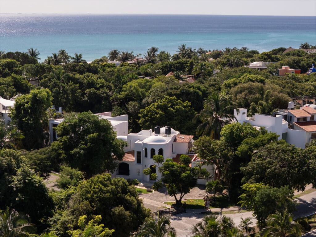 An aerial view of Casa Marita in Playacar Phase 2, Playa del Carmen, showing a white Mediterranean-style house surrounded by lush greenery and with a view of the ocean in the distance.