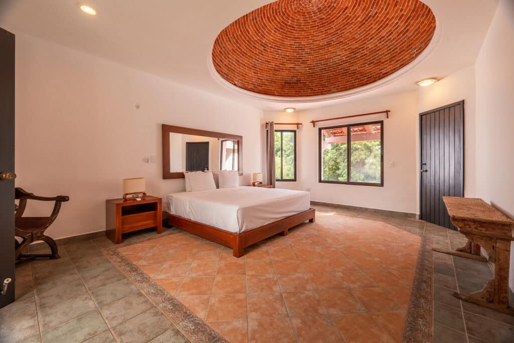 Interior view of Casa Marita in Playacar Phase 2, Playa del Carmen, showcasing a spacious bedroom with a circular brick ceiling feature, wooden furniture, and large windows.