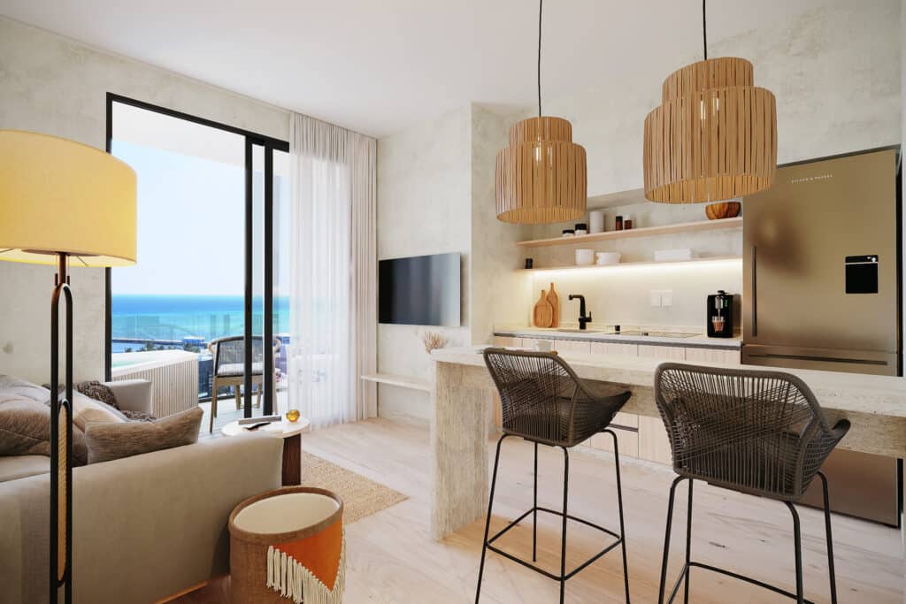 Interior view of Petrus in Playa del Carmen, featuring a modern living area with a balcony overlooking the ocean, an open kitchen with wooden pendant lights, and stylish furnishings.