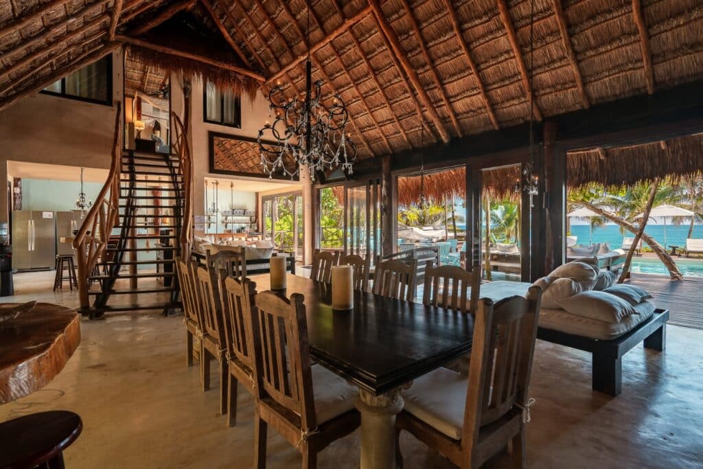 Interior view of Casa Chic, a beachfront home in Tulum, showcasing a spacious, rustic-style dining area with large windows and an outdoor patio overlooking the ocean.
