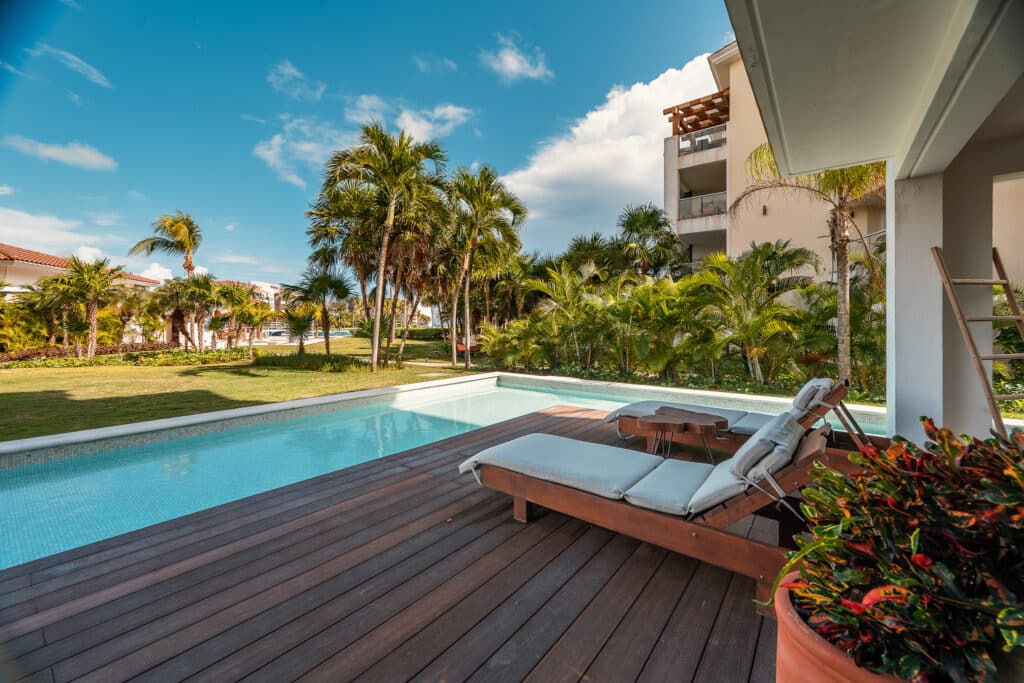 A spacious outdoor area with a pool, wooden deck, and lounge chairs at Mareazul 401 Sur in Playa del Carmen's Corasol area, surrounded by palm trees and lush greenery.