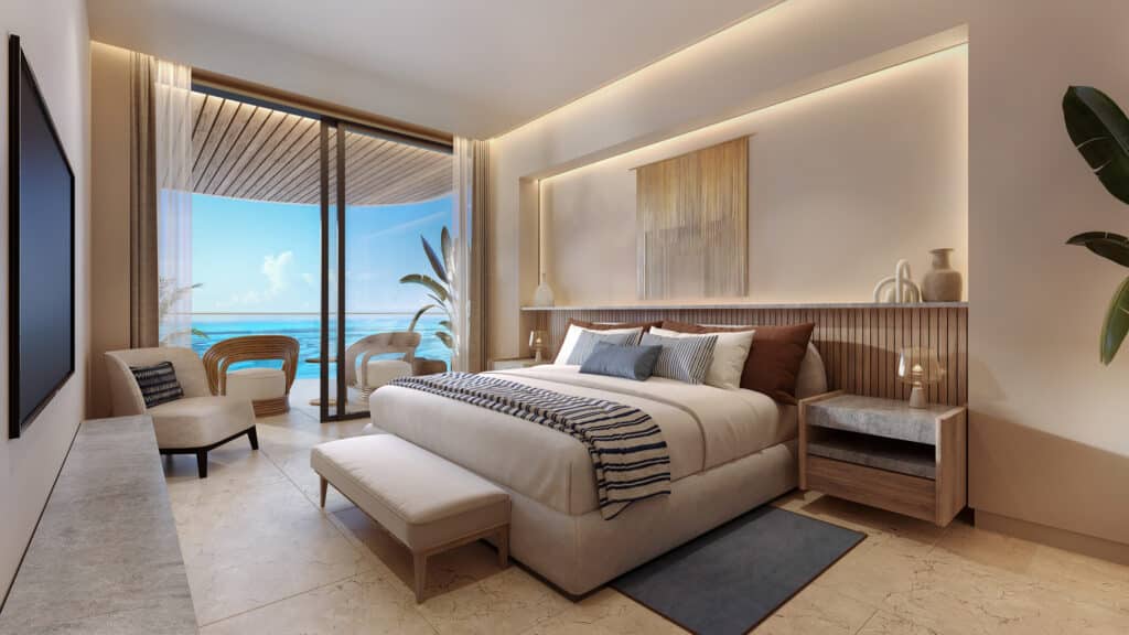 A modern bedroom at Marietta Residences in Isla Mujeres features a large bed with striped and solid pillows, a bench at the foot, and a balcony with ocean views.