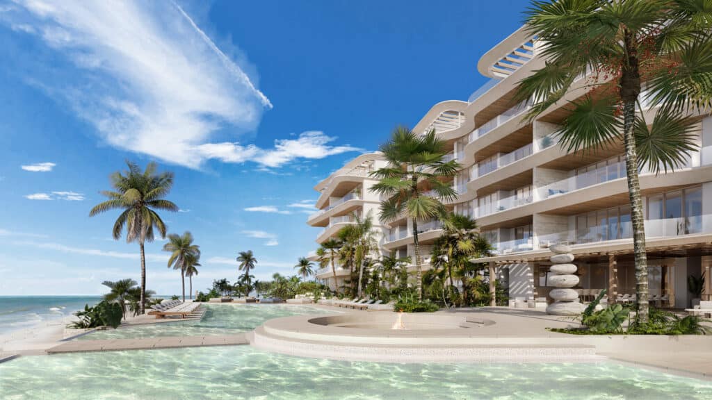 A modern beachfront condominium at Marietta Residences in Isla Mujeres features a curved building design, tall palm trees, a swimming pool, and a sunny sky.