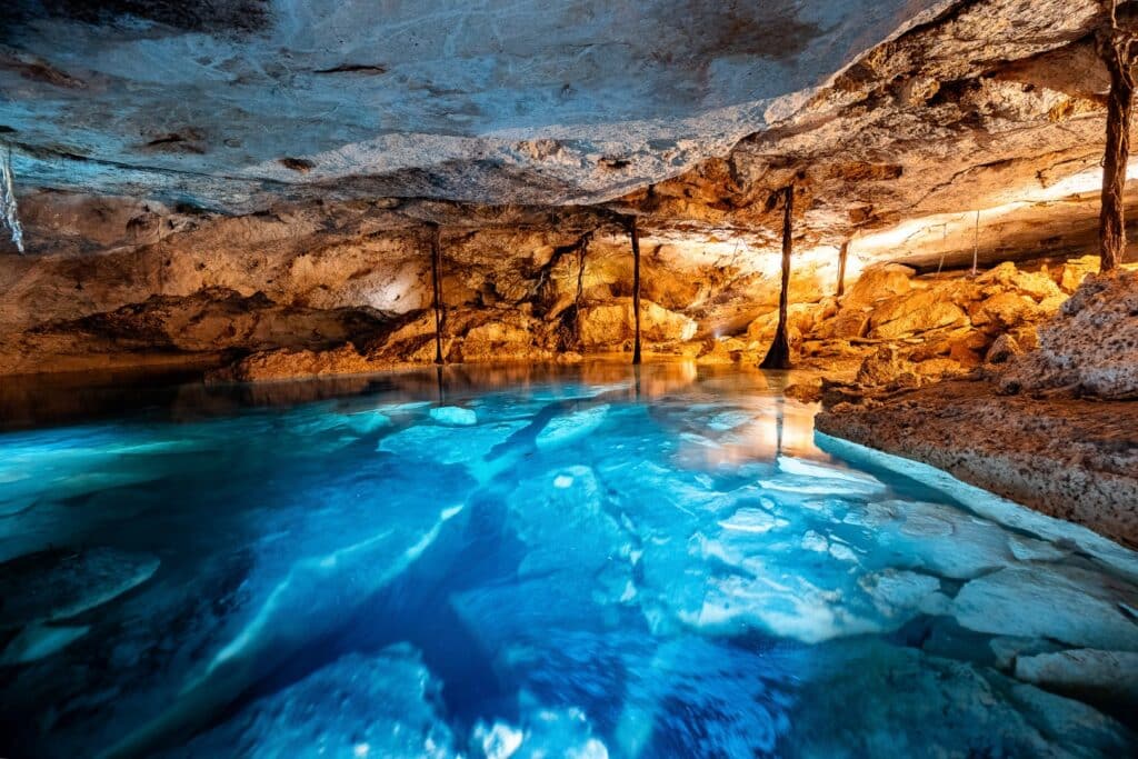 Interior of a cave with a pool of water, illuminated by warm lighting, near Akumal in Rancho San Martin.