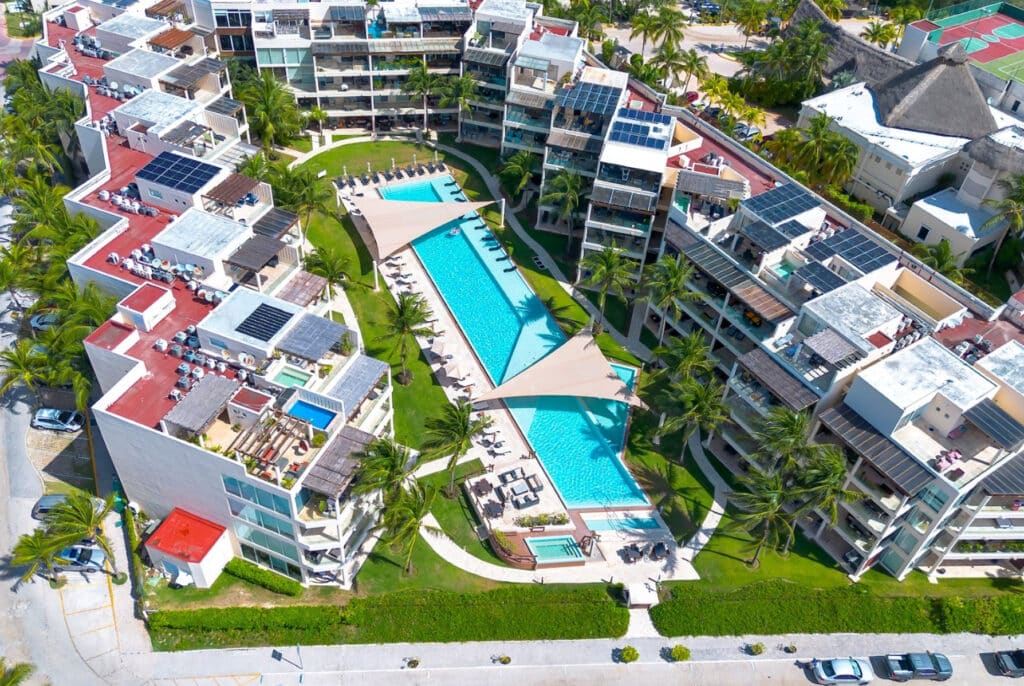 Aerial view of The Elements in Playa del Carmen's Coco Beach area, showcasing modern condos surrounding a large swimming pool with lounge areas and lush landscaping.