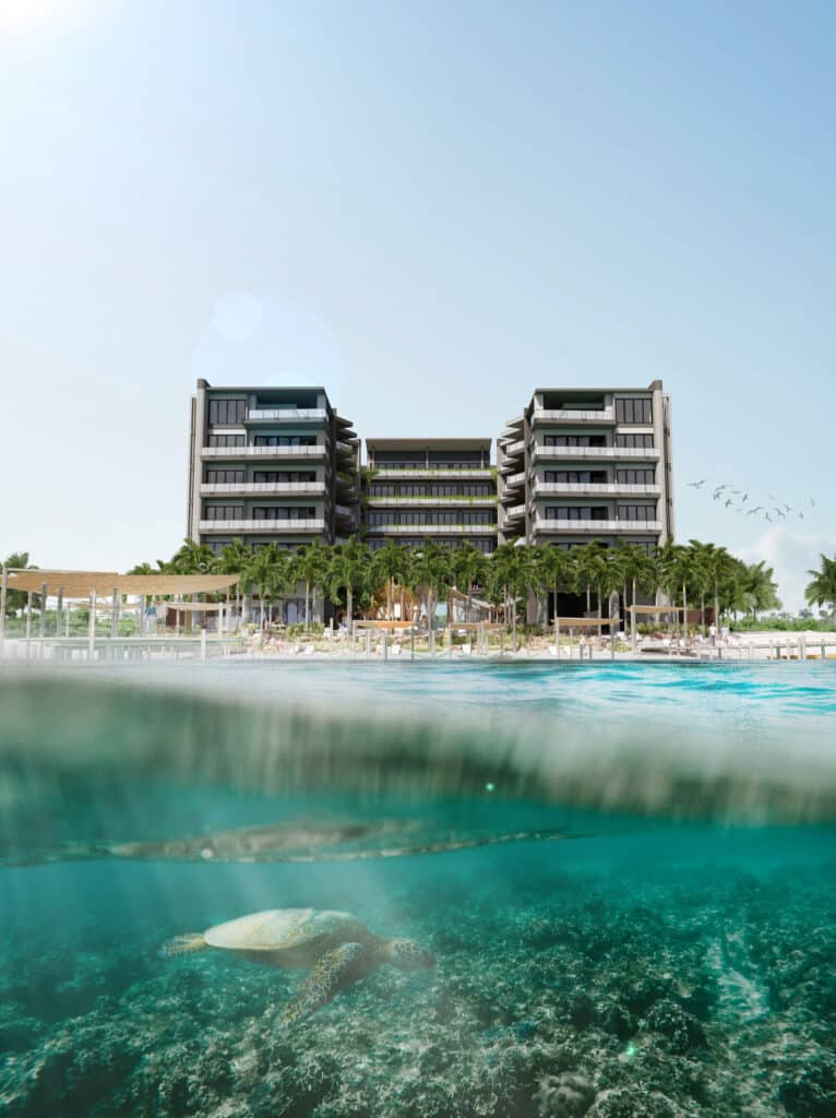 A modern beachfront condo building at Belmare in Tulum, with palm trees lining the property and a turtle swimming underwater in the foreground against a clear sky.