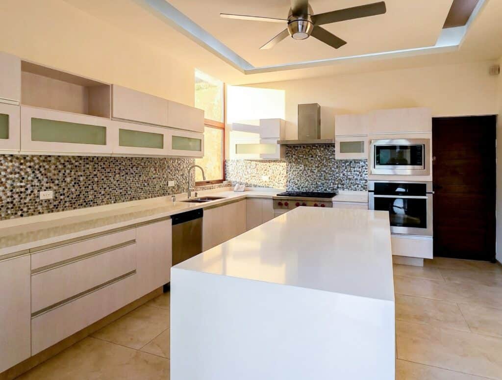 Modern kitchen in Bosques De Altabrisa, Merida, featuring white cabinetry, a mosaic backsplash, and built-in appliances with ample natural light.