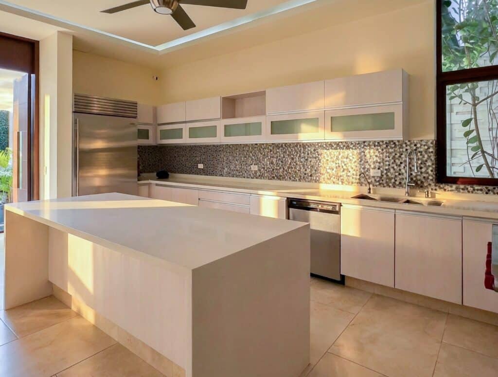 Modern kitchen in Bosques De Altabrisa, Merida, featuring white cabinetry, a mosaic backsplash, an island, and large windows bringing in natural light.