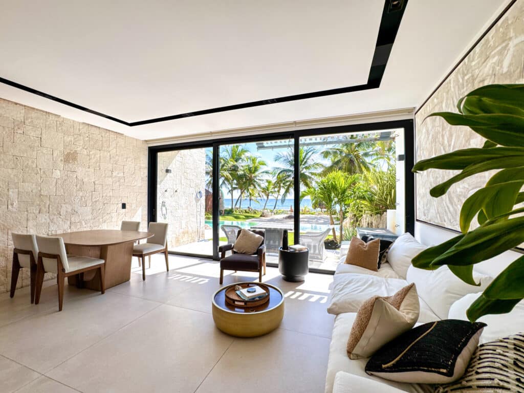 Interior view of CasaCún beachfront condo in Puerto Aventuras with large sliding glass doors opening to a tropical pool area and ocean beyond.