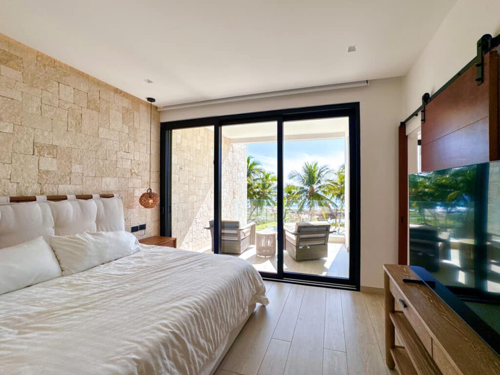 Bedroom in CasaCún beachfront condo in Puerto Aventuras with a sliding door leading to a balcony overlooking palm trees and the ocean.
