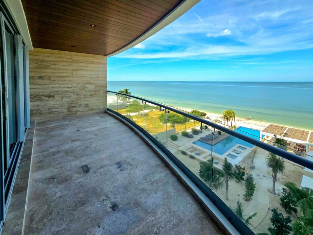 Balcony of Catavento A-41 in Progreso, overlooking the beachfront with views of the pool, palm trees, and the ocean under a partly cloudy sky.