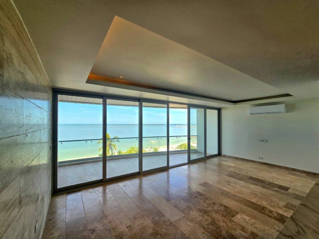 Interior view of a beachfront condo at Catavento A in Progreso, featuring large glass doors opening to a balcony with ocean views and a modern ceiling design.