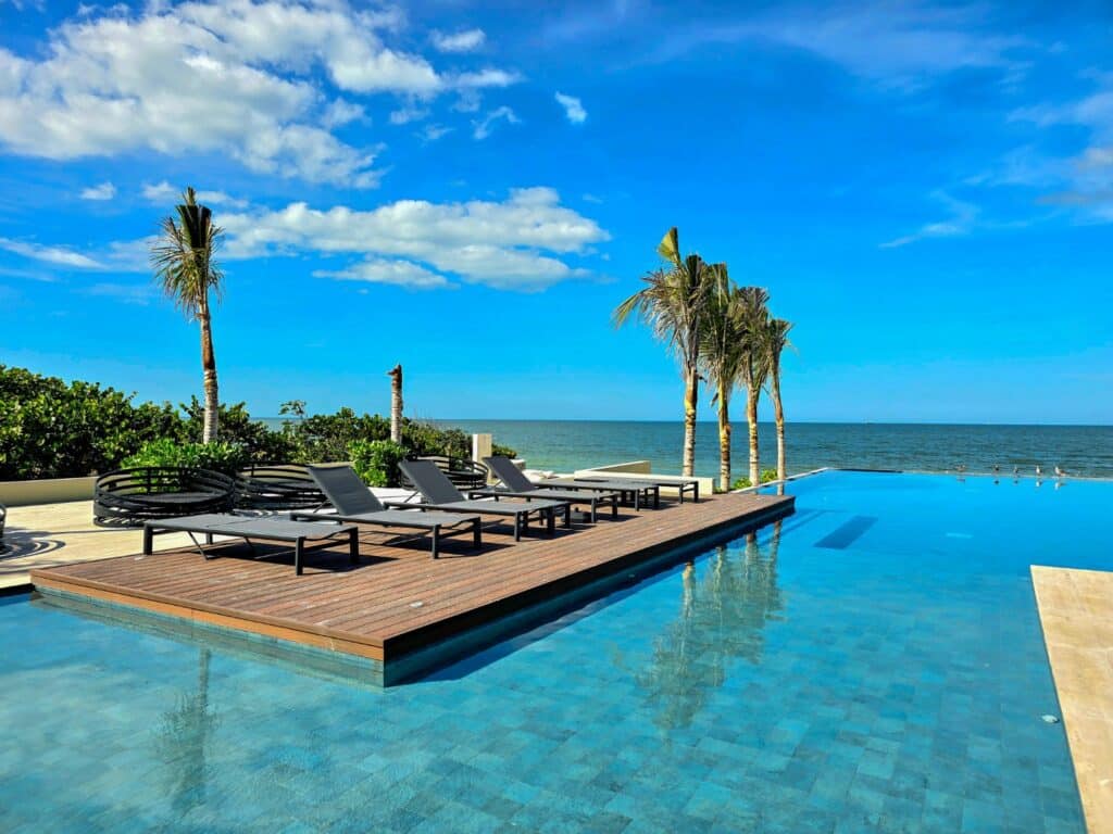 Pool area with lounge chairs overlooking the ocean at Catavento A-41 in Progreso's beachfront development with palm trees and blue sky.