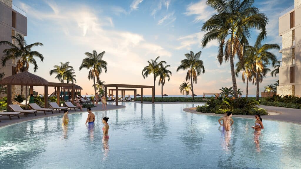 Dunas in Chuburna is a beachfront development with a swimming pool area surrounded by palm trees and sun loungers, overlooking the ocean at sunset.