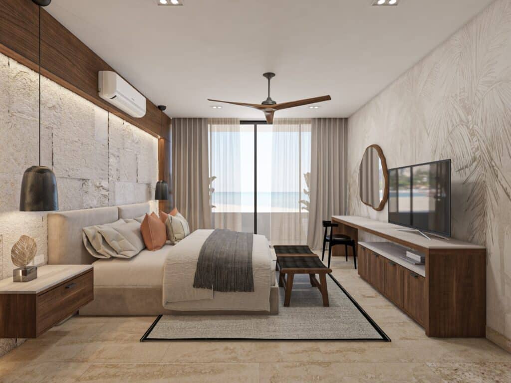 A modern bedroom in Madeira Vida De Mar, Chicxulub, with a view of the beachfront, featuring a bed with colorful pillows, wooden furniture, a TV, and glass doors leading to a balcony.