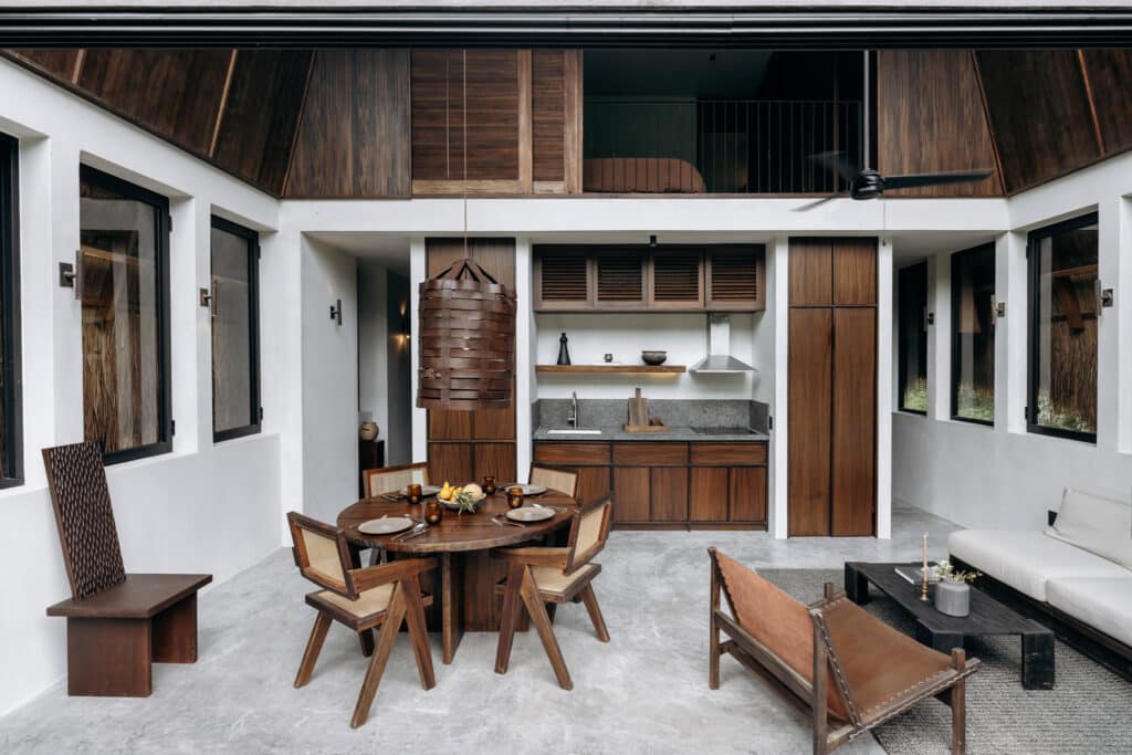 Interior of Casa Kuro 203 in Tulum's Region 15, featuring a modern kitchen with wooden cabinets, a dining area with a round table, and a white sofa in a spacious living space.
