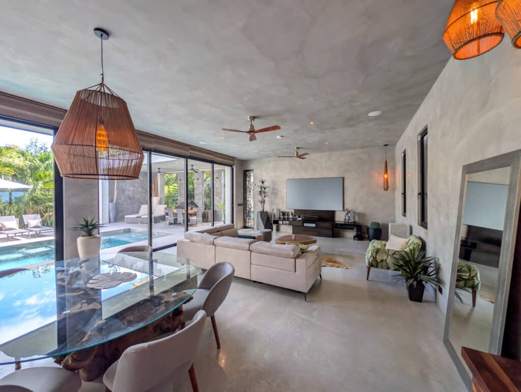 Interior view of Casa Luum House in Playacar Phase 2, Playa del Carmen, showcasing a spacious living area with a large beige sofa, modern decor, a glass dining table, and sliding.