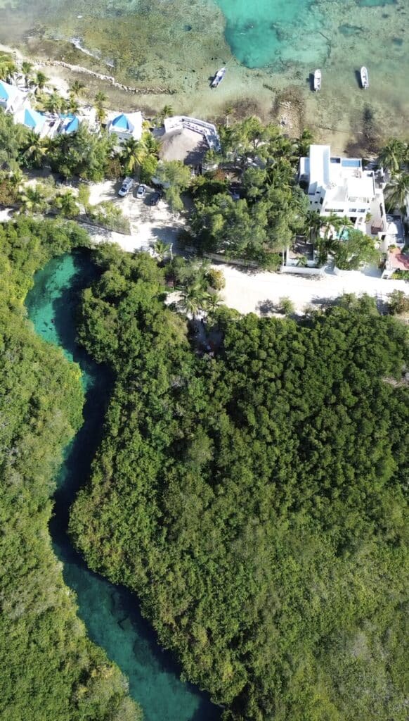 Aerial view of a beachfront property at Tankah Bay Tulum Beachfront in Tulum, showing white buildings, lush greenery, and clear turquoise waters along the coast.