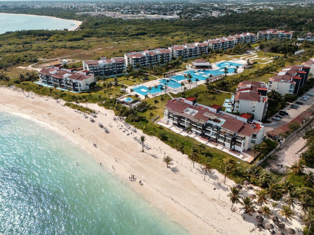 Aerial view of Mareazul 332N in Corasol, Playa del Carmen, showing beachfront buildings, multiple swimming pools, and landscaped gardens adjacent to the sandy shoreline.