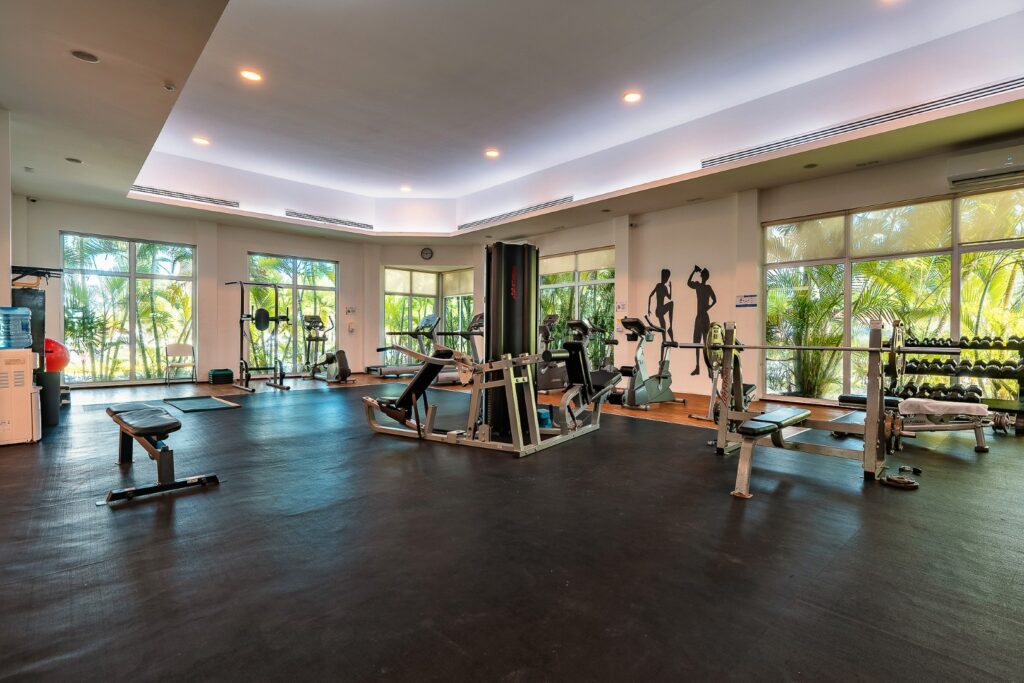 Fitness center at Mareazul 332N in Playa del Carmen, with large windows showing lush greenery and modern exercise equipment on a dark wood floor.