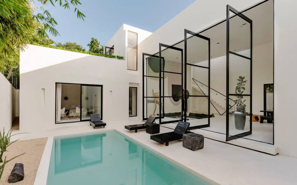 Modern white villa with a swimming pool and black-framed glass doors in Aldea Zama, Tulum.