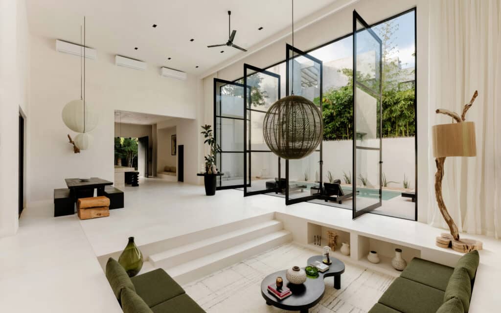 Living area of Villa Coco Dar Lalla in Aldea Zama, Tulum, featuring a modern design with large glass doors leading to an outdoor space and a neutral color palette.