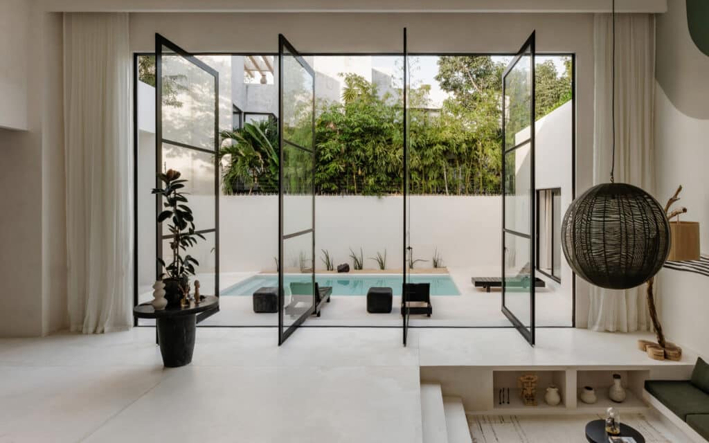 A view through glass doors overlooking a small pool and lush greenery at Villa Coco Dar Lalla in Aldea Zama, Tulum.