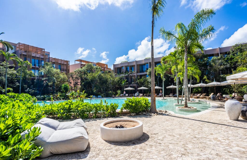 Luxury pool area with sun loungers, lush greenery, and modern residential buildings in the background in Tulum at Aflora.